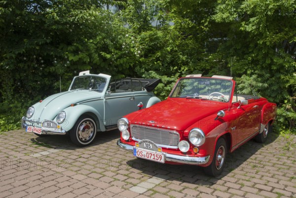 Two classic convertibles, one red and one light blue, parked next to each other on a paved car