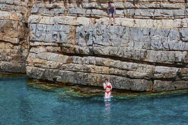 Palatia Beach, Palatia, A person jumps from a rocky cliff into the turquoise water, another person
