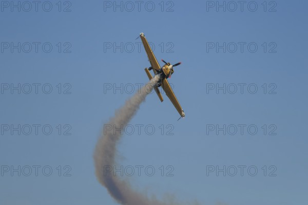 Golden stunt aerobatic plane performing stunts in blue sky with smoke trail. Concept of speed,