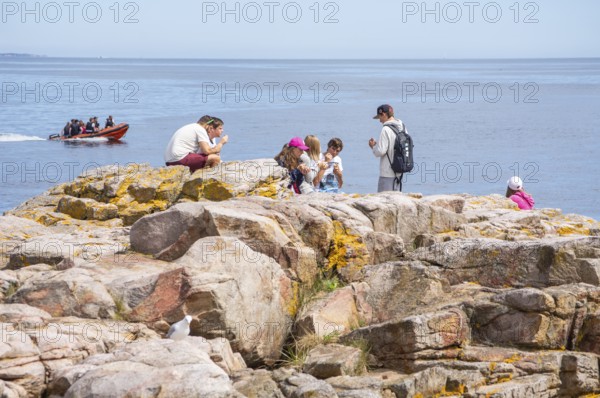 People on rocks by the sea with speedboat in the background in Gudhjem, Bornholm, Baltic Sea,