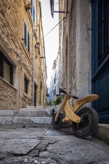 A child's bike stands in a sunny, historic alley with stone steps, Korcula, Croatia, Europe