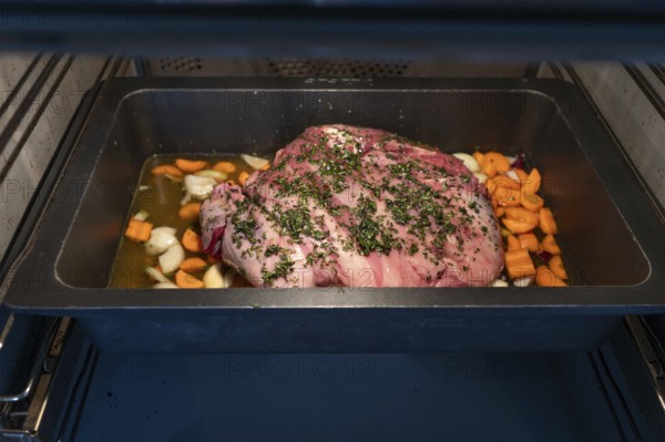 Preparation of a wild boar roast with spices and vegetables in a cast-iron casserole in the oven,