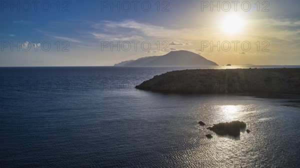 Sunset over the sea with a visible island and calm water, Kassos Island, drone shot, evening light,