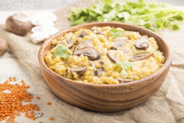 Lentils porridge with champignons and coriander in a wooden bowl on a white wooden background and