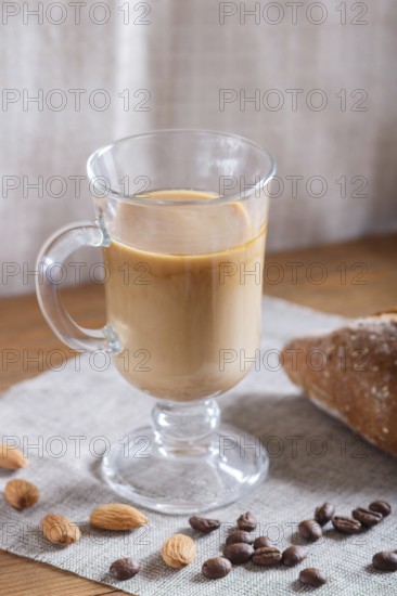 Glass cup of coffee with cream and bun on a wooden background and linen textile. close up