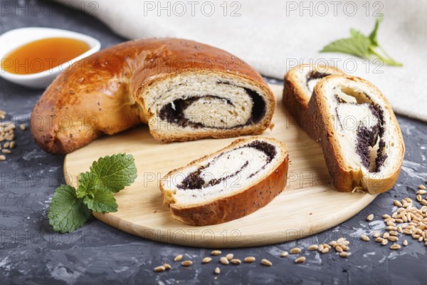 Homemade yeast rolls with poppy seeds and honey on a wooden kitchen board on a black concrete