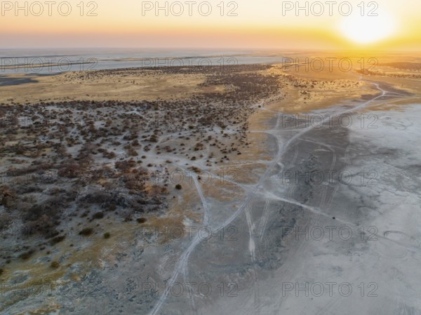 Rocky island with baobab trees in a dry salt pan, at sunset, off-road vehicle on the salt pan,