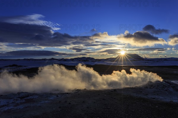 Hot springs and geothermal area in front of mountain landscape in winter, sunbeams, cloudy mood,