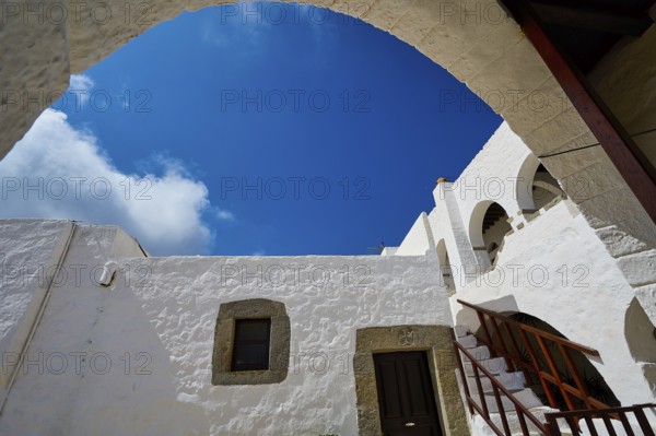 View from below of white buildings and a staircase under an arch in the Greek monastery, Inside the