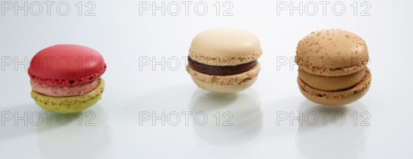 Three differently coloured macarons in front of a white background, studio shot