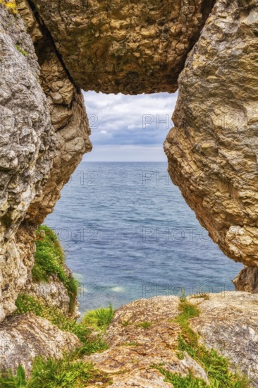 Rock opening overlooking the calm sea under a cloudy sky, Ballycastle