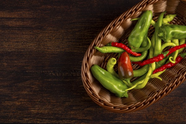 A brown basket with green and red peppers on a wooden base