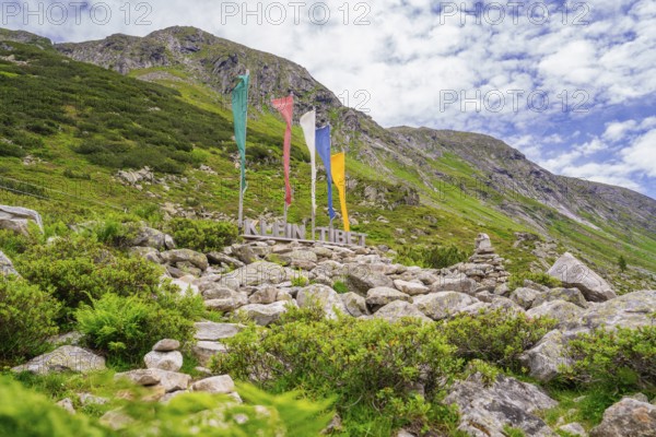 Landscape in the mountains with colourful flags, a sign and green vegetation, framed by rocks,