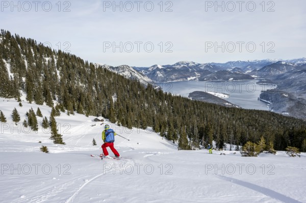 Skiers skiing down the Simetsberg, view of Walchensee and mountain panorama, Estergebirge, Bavarian
