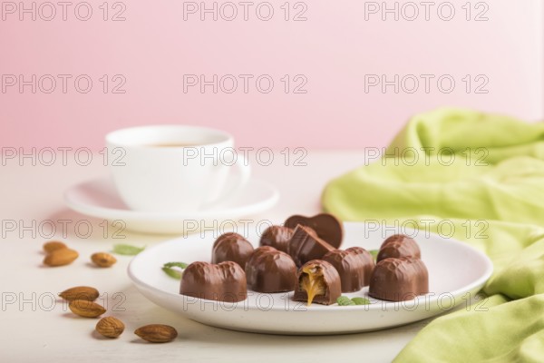 Chocolate caramel candies with almonds and a cup of coffee on a white and pink background and green