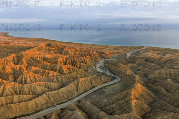 River bed runs through a landscape of eroded hills, badlands at sunset, Lake Issyk Kul in the