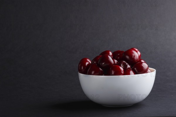 Fresh red sweet cherry in white bowl on black background. side view, copy space