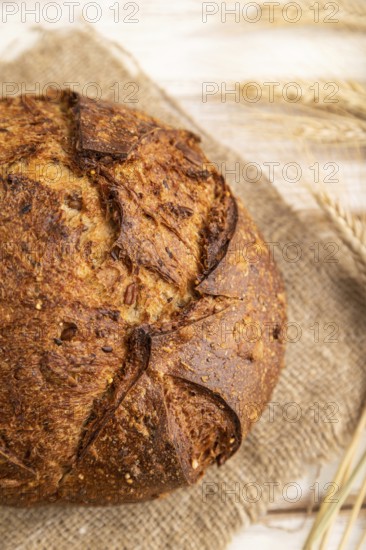Fresh homemade golden grain bread with ears of wheat and rye on white wooden background and linen