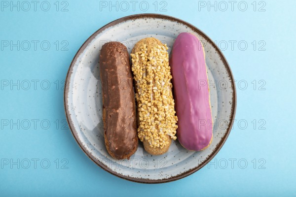 Set of eclair, traditional french dessert on ceramic plate on blue pastel background. top view,