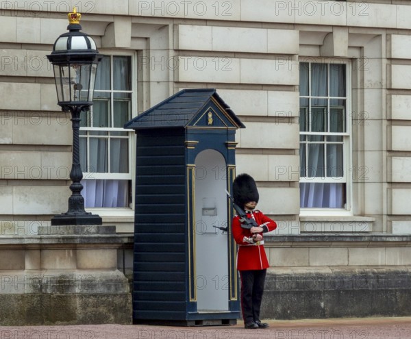 A guard in red uniform stands in front of a guardhouse next to a lantern at Buckingham Palace,