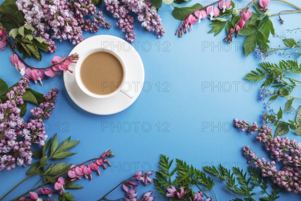 Purple lilac and bleeding heart flowers and a cup of coffee on pastel blue background. Morninig,