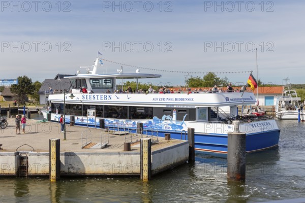 A large passenger ship with a flag is moored at the jetty in the sunny harbour, Rügen, Hiddensee