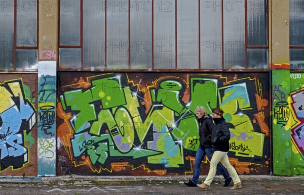 Two people walking along a wall covered with colourful graffiti, urban ambience, Landau,
