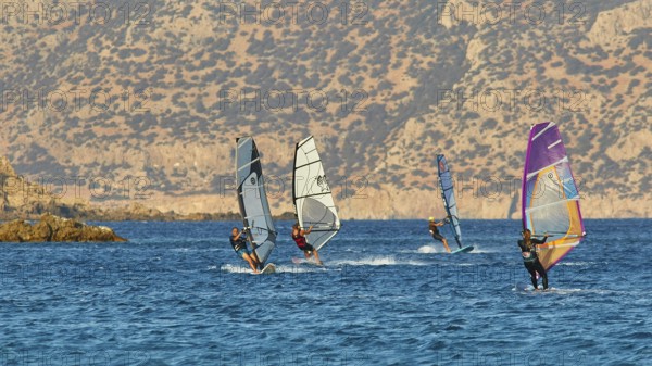 Windsurfers enjoy the sunny weather on the blue sea in front of a rocky coast, windsurfers, Meltemi