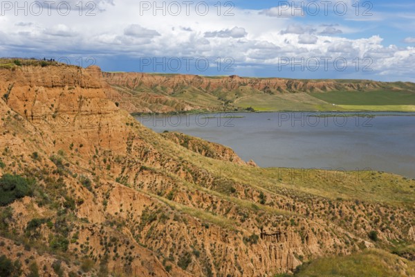 Ein felsiger Canyon, der sich entlang eines Sees erstreckt, unter einem überwiegend blauen Himmel