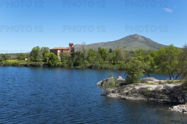 Clear lake next to a building, surrounded by nature and mountains under a blue sky, palace, Palacio