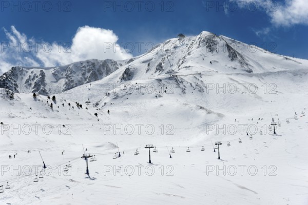Schneebedeckte Berge unter blauem Himmel, mit Skiliften und einigen Skifahrern auf den Pisten,