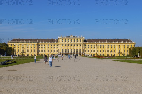 Schönbrunn Palace with yellow facade and blue sky in the background, some tourists in the