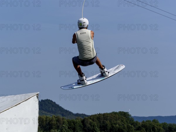 Young man jumping with wakeboard over jump and obstacle, water sports, water skiing in wakepark,
