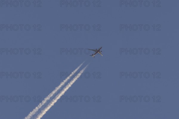 Boeing 787-8 Dreamliner aircraft flying across a blue sky with a vapour trail or contrail behind,