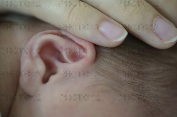 Close-up of a baby whose ear is gently touched by a hand