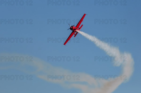 Red stunt aerobatic plane performing stunts in blue sky. Concept of speed, difficulty, precision,