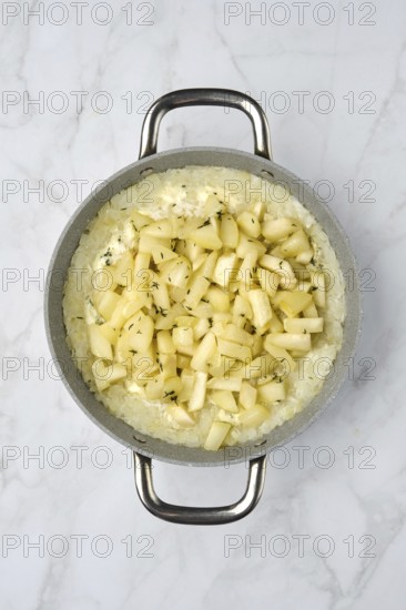 A silver pot filled with creamy rice topped with freshly diced pears and herbs on a marble