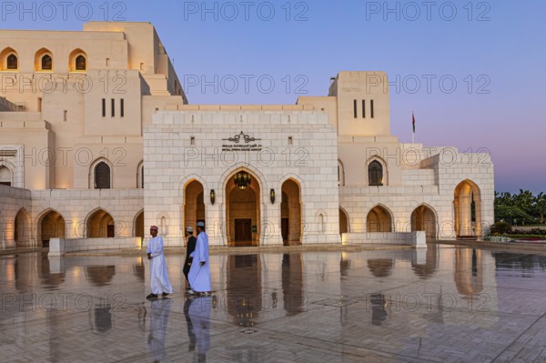 Local men walk across the main square in front of the Royal Opera at the blue hour, Muscat, Arabian