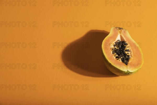 Ripe cut papaya on orange pastel background. Side view, copy space, hard light. Tropical, healthy