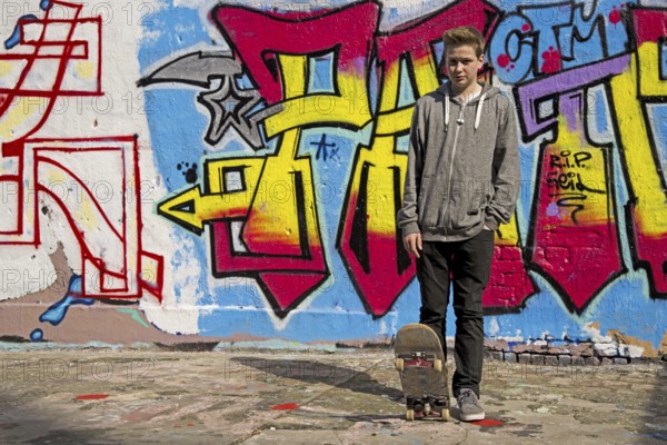Thirteen-year-old boy with skateboard in front of graffiti, Cologne, Germany, Europe