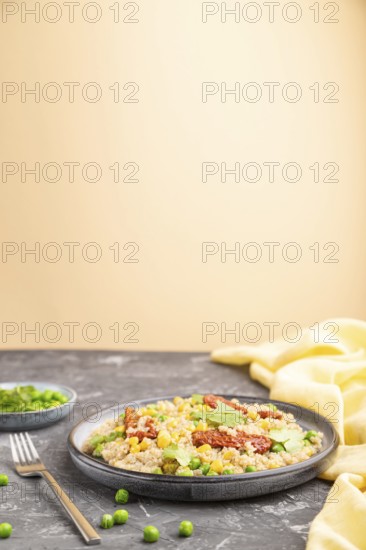 Quinoa porridge with green pea, corn and dried tomatoes on ceramic plate on a gray and orange