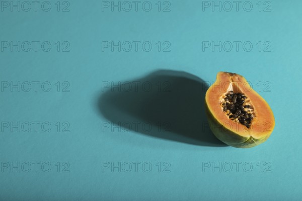 Ripe cut papaya on blue pastel background. Side view, copy space, hard light. Tropical, healthy