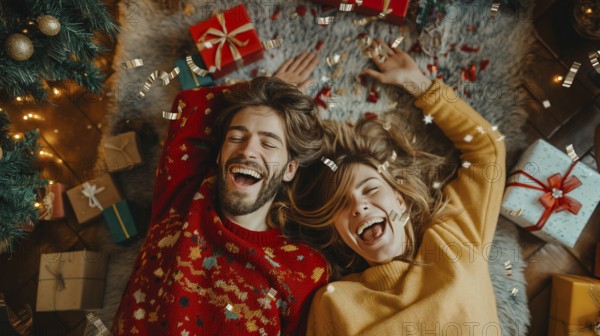 Young couple laying on their backs surrounded by christmas gifts and decorations laughing.