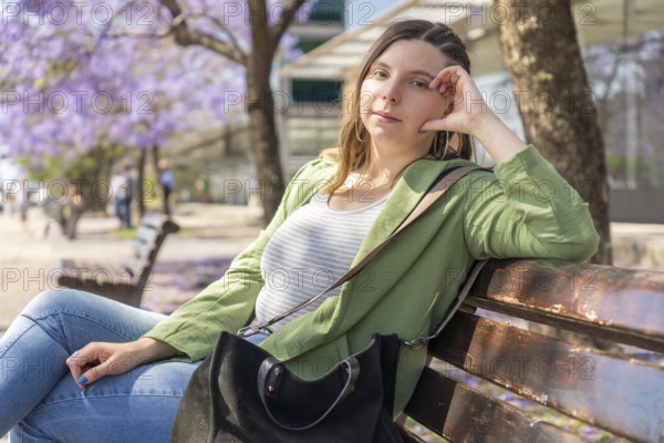 A young woman in a green jacket looks at the camera while sitting relaxed on a bench under purple