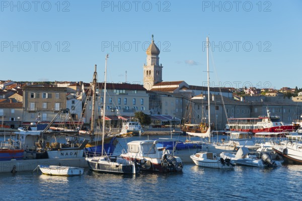 Coastal town at sunset with harbour and boats, in the background a church and historical buildings,