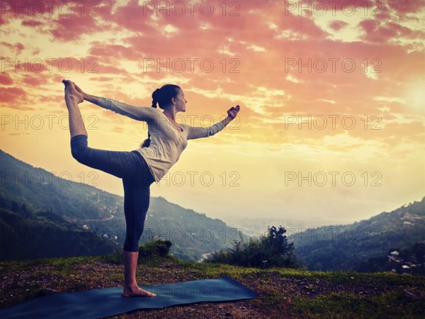 Woman doing yoga asana Natarajasana, Lord of the dance pose outdoors at waterfall in Himalayas.