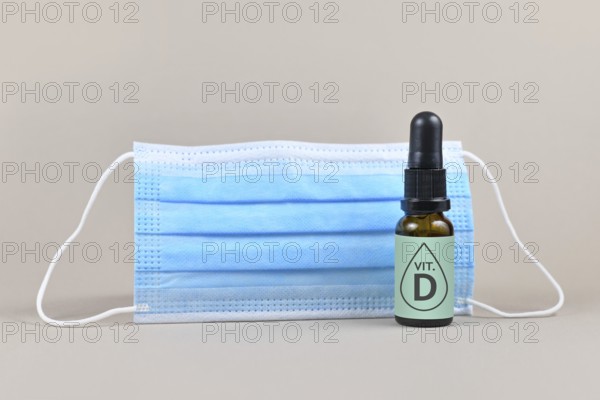 Medical face mask and bottle with vitamine drops on gray background