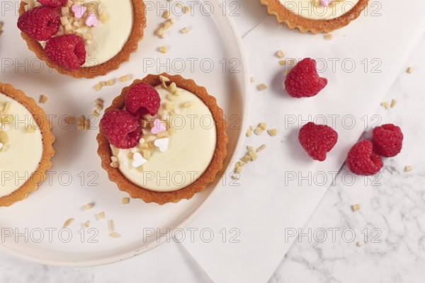Top view of small tartlet pastries with white cream, topped with raspberry fruits and almond