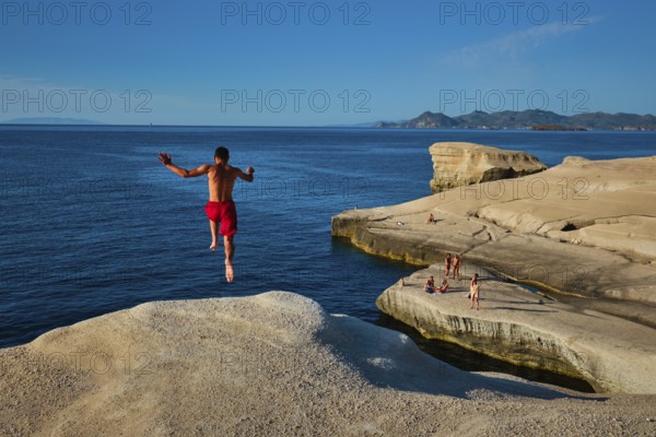 Sarakiniko, Greece, May 23, 2019: Young tourists jump off the white rocks cliff on famous tourist