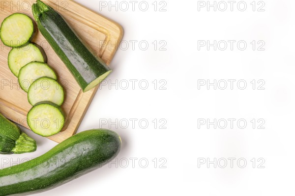 Courgettes (Cucurbita pepo), whole and cut open, on wooden board, on white, copy room